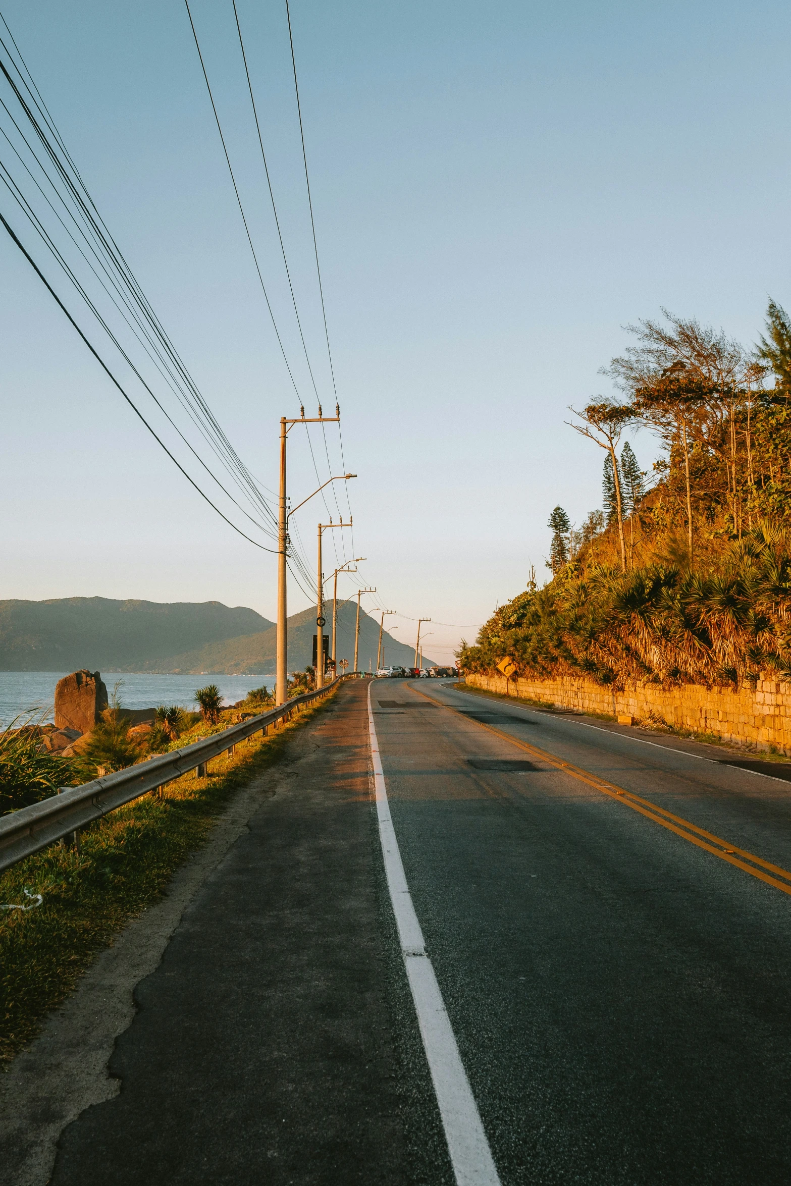 a long street with power lines overhead and a view of a lake