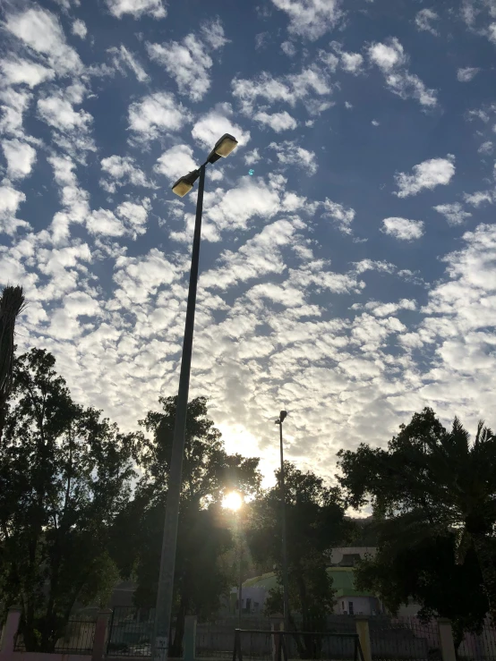 sun shining through clouds near buildings with light posts