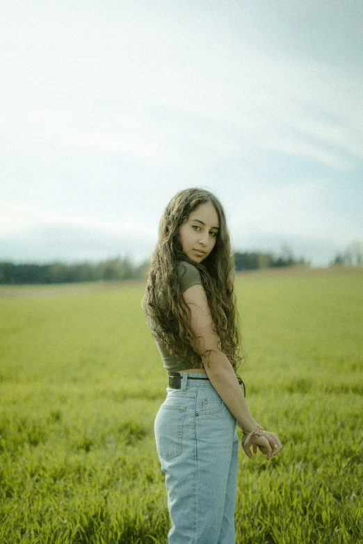 a girl standing in a large field looking at the camera