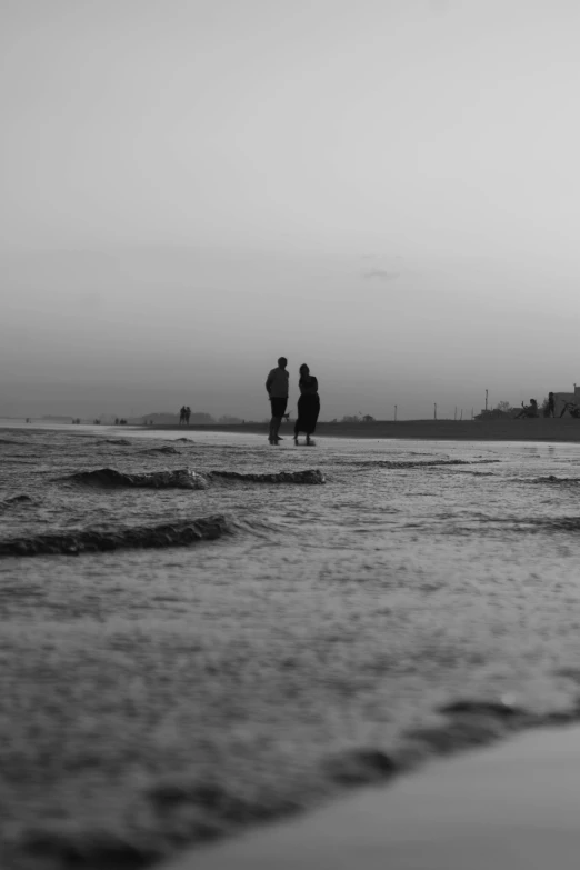 two people standing in the water looking out to sea