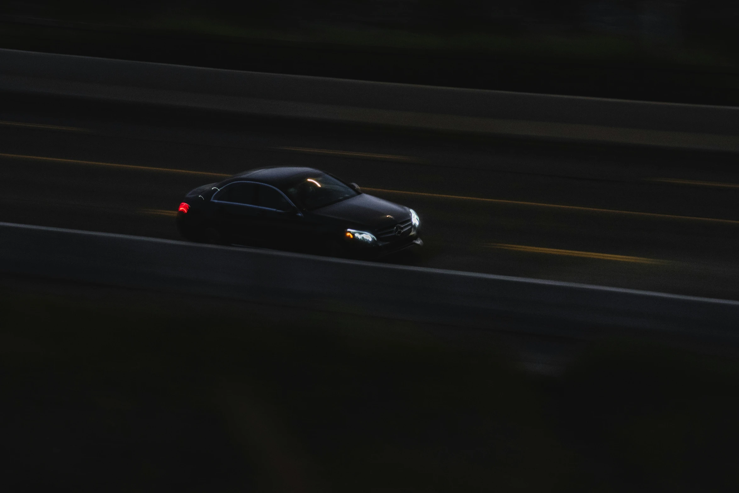 the front end of a small black car driving on a road