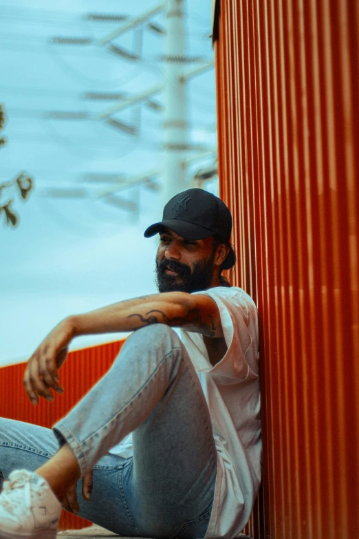 man sitting next to red building with his legs crossed