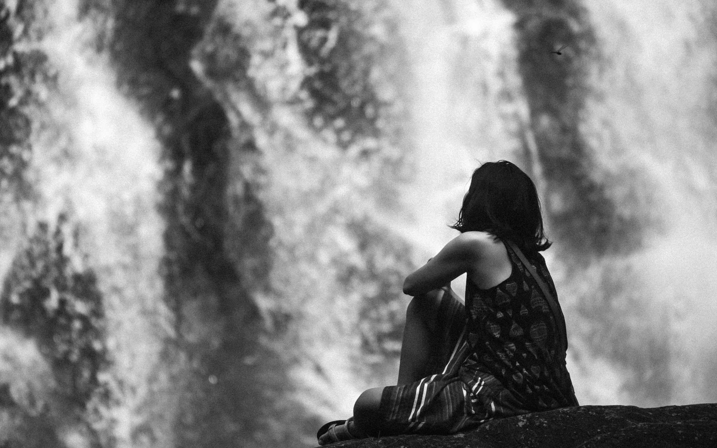 a woman sitting on top of a rock next to a waterfall