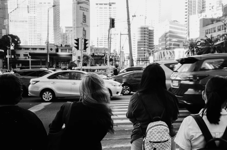 group of people waiting at a crosswalk on a busy city street