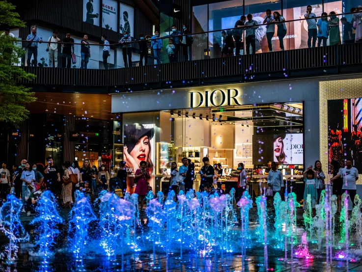 several people are standing around water fountains outside