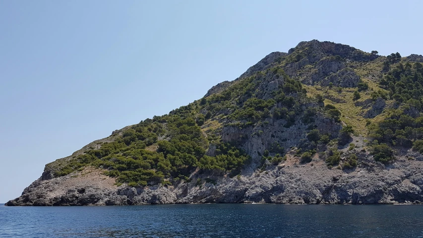 a mountain rises above the water in front of the blue sky