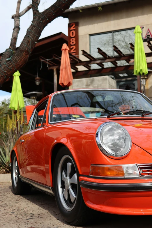 an orange car parked outside a restaurant in front of green umbrellas