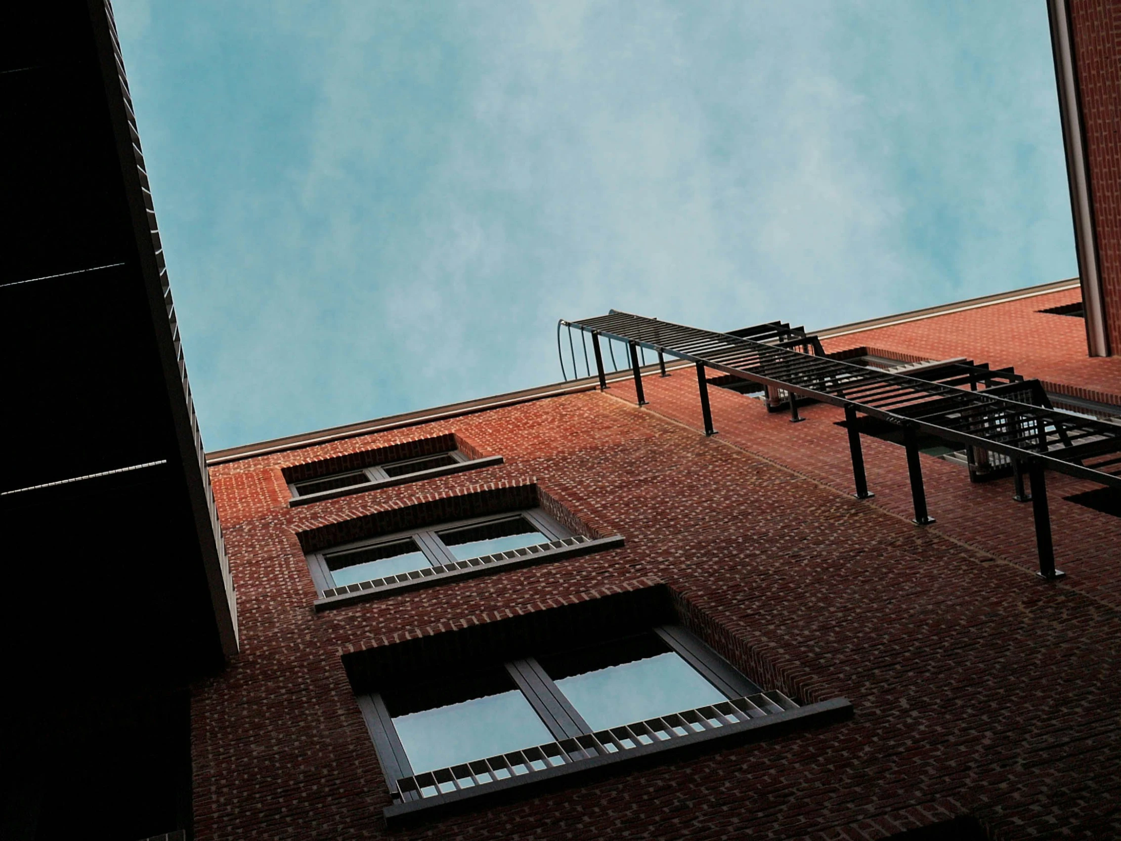 the back of a red brick building with windows in the sunlight