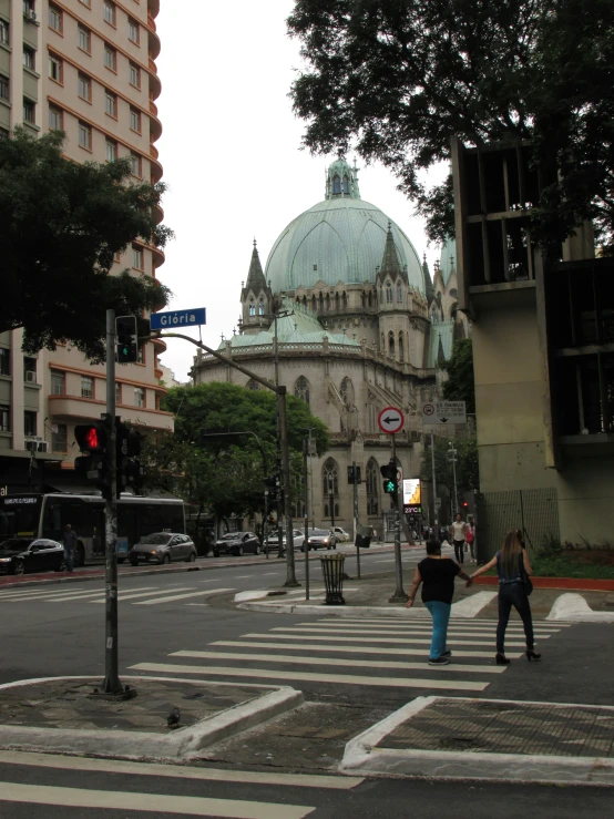 two people crossing at an intersection in front of large buildings