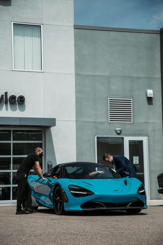 a man on a motorcycle stands next to a blue car