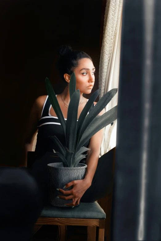 a young woman sits in a chair near a plant