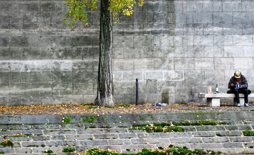 a woman is sitting alone on a concrete bench near a tree