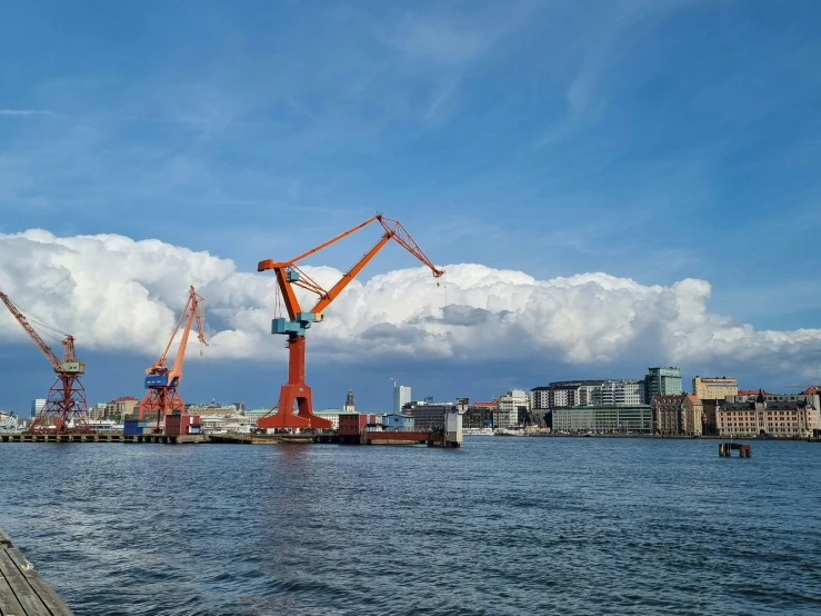 cranes sit on land by the water and some buildings