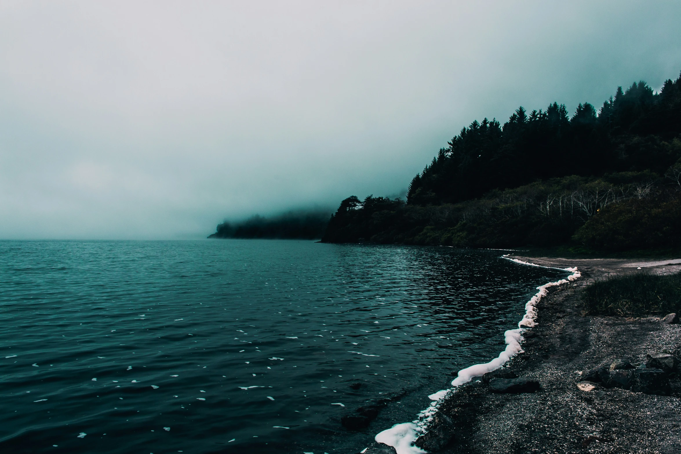 an ocean view with fog on the water and clouds hovering over the water