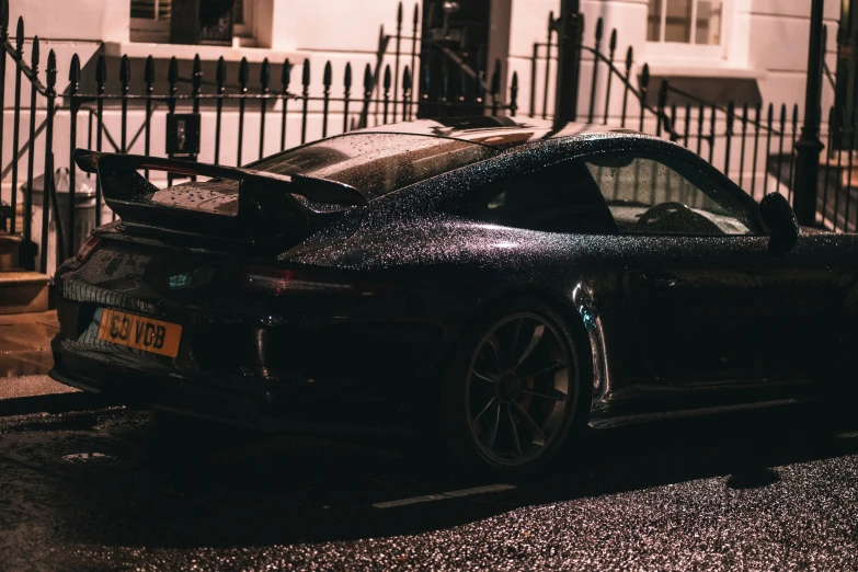 a dark car with its lights on and some snow on it