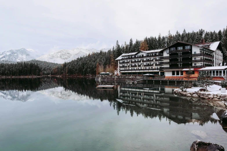 the building is along the lake with mountains in the background