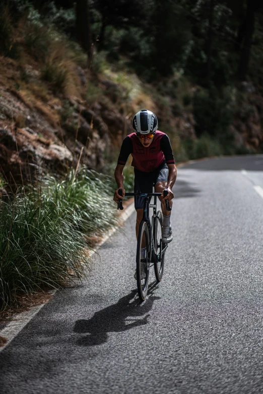 a man on a bicycle riding down a road with grass and trees