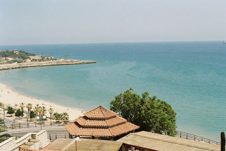 a beach with blue water, and brown tiled roofs