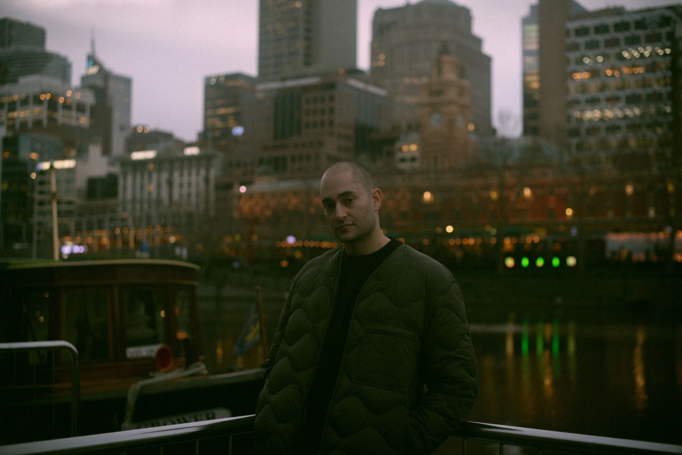 a man in a black jacket stands in front of some buildings in the city