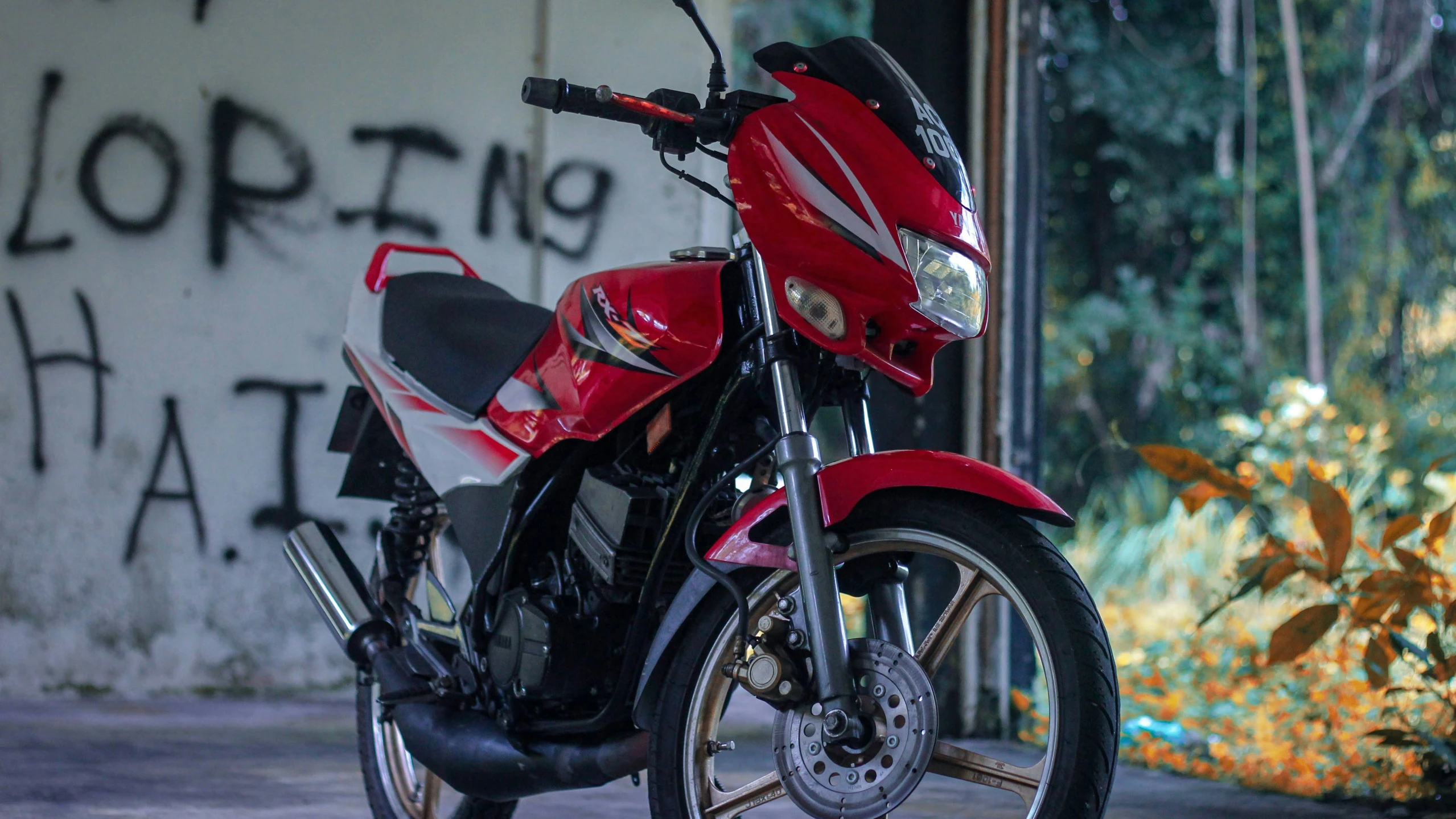 a red motorcycle parked next to a bush and building