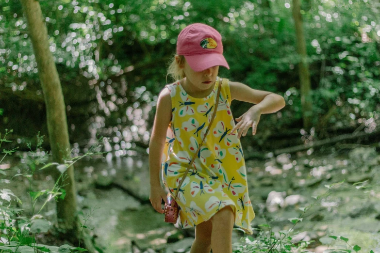 girl in yellow dress and pink hat walking across grass