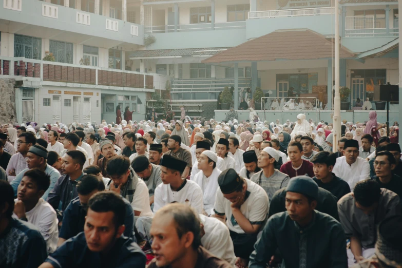 a crowd of men sit in rows outside buildings