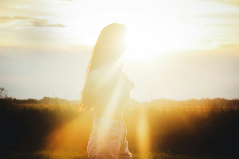 a woman walking in a field with the sun glaring through her long hair