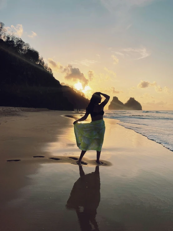 woman standing on the beach at sunrise holding her sheered dress over her head