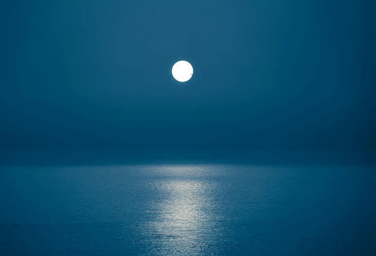 a full moon shining over the ocean on a night
