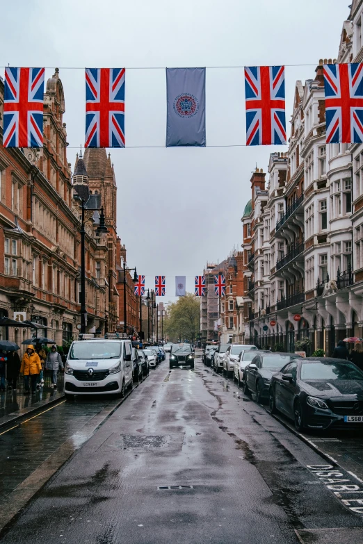 cars line a wet city street under the british flag banners