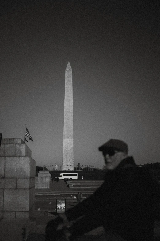 a man sitting outside near a monument with a hat on