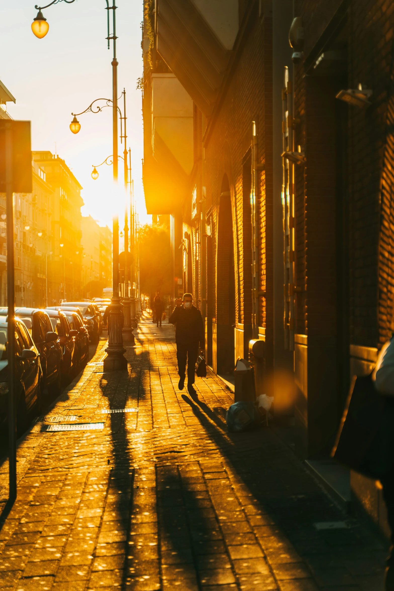 the sun rising over a brick sidewalk near street lamps