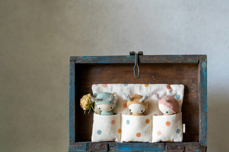 three small little knitted dolls sitting in an old suitcase