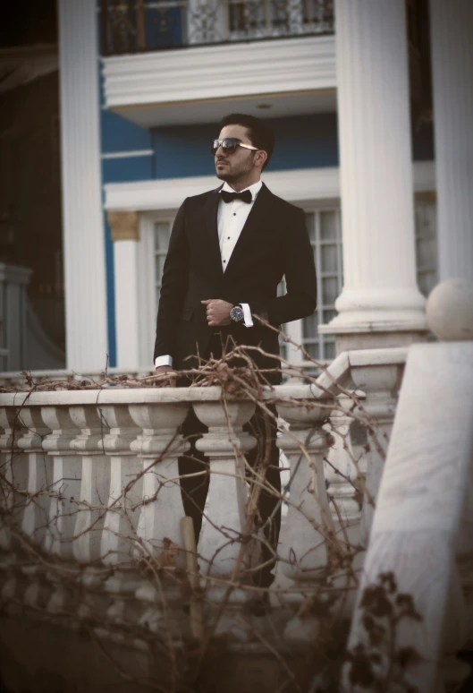 a man in a tuxedo leaning against a railing