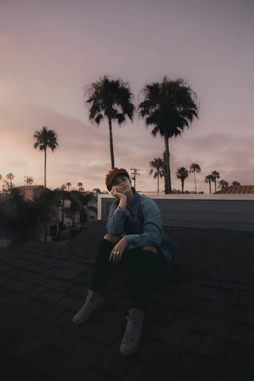 a man sitting on a roof at sunset with his hand to his mouth