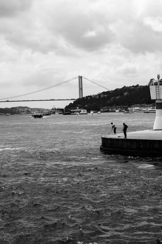 people running near the water with a suspension bridge behind them