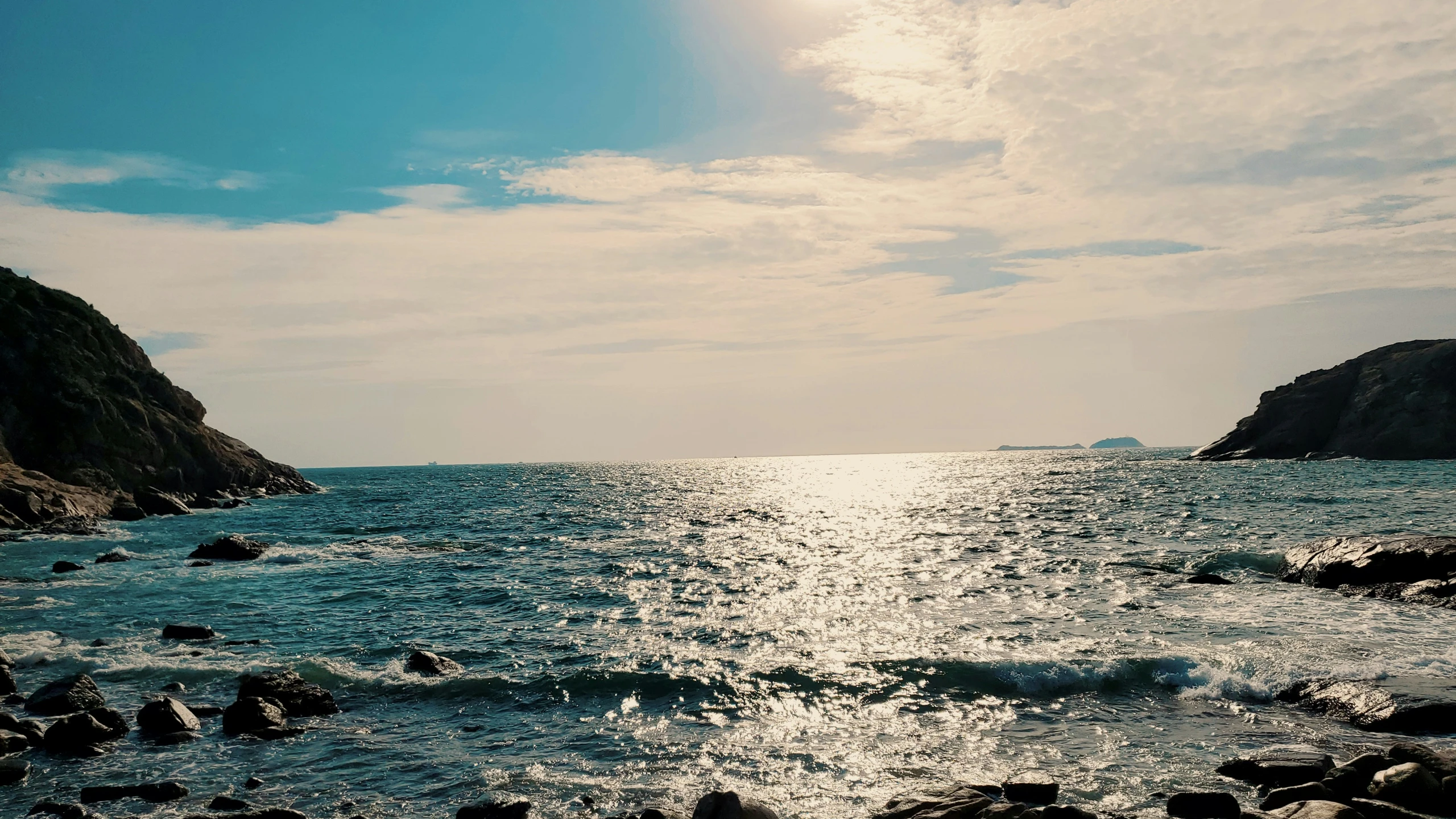 the sun reflects off of the water next to a rocky shore