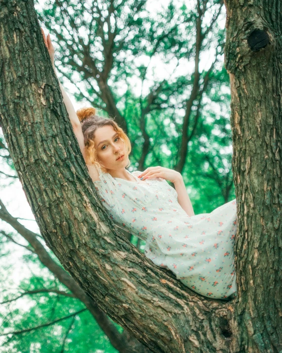 young woman wearing white dress sitting on a tree nch