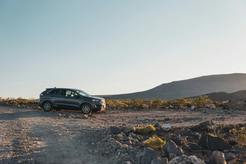 a small vehicle driving in the desert, with mountains and bushes