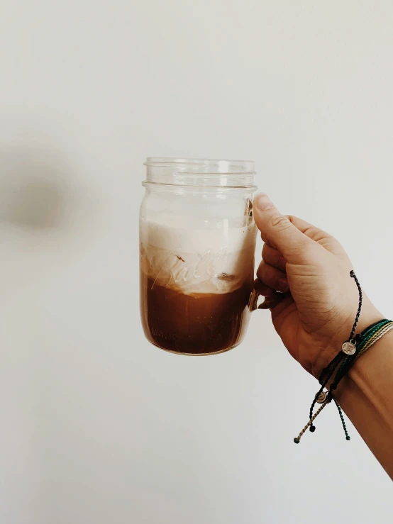 hand holding a jar filled with liquid against a white wall