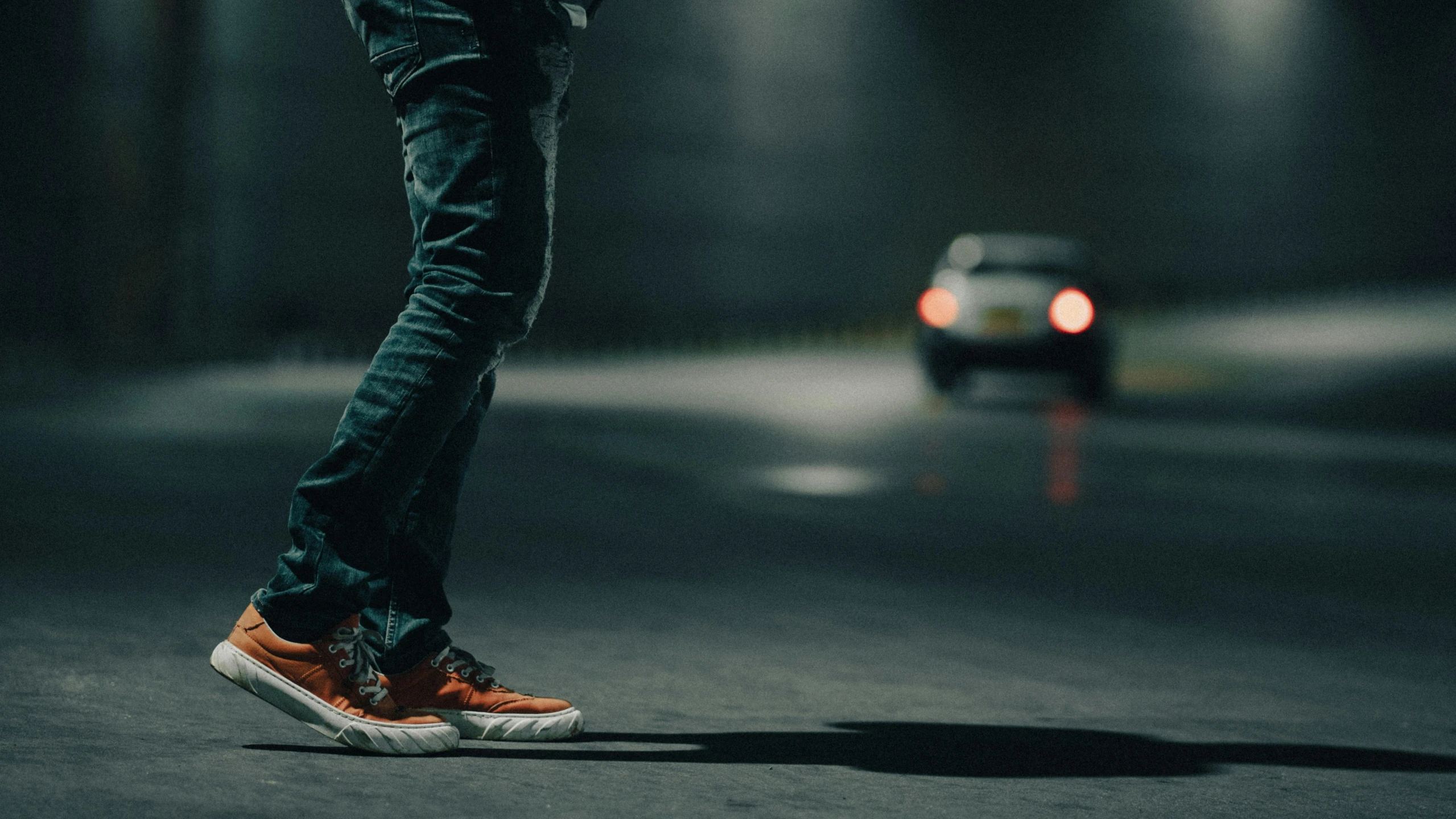 a man is standing on a road with a car in the distance