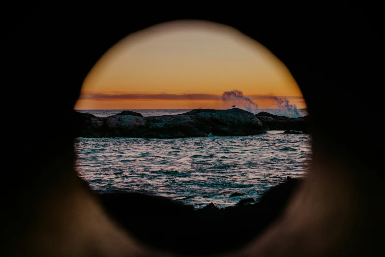 a view through a porthole of the ocean at sunset