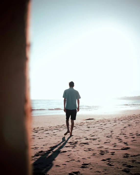 man in white shirt on beach next to wall and ocean