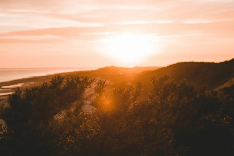 sunset over a hill next to ocean