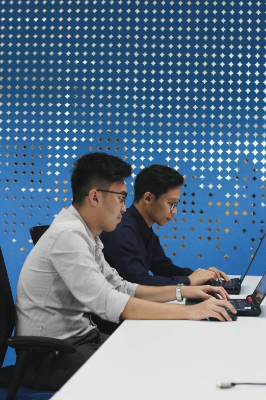 two men sitting at a table with laptop computers in front of them