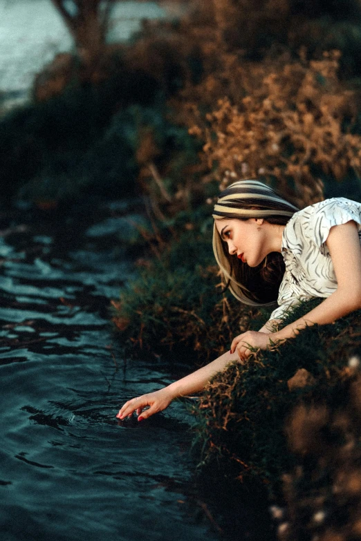 woman with freckled shirt touching the ground near water