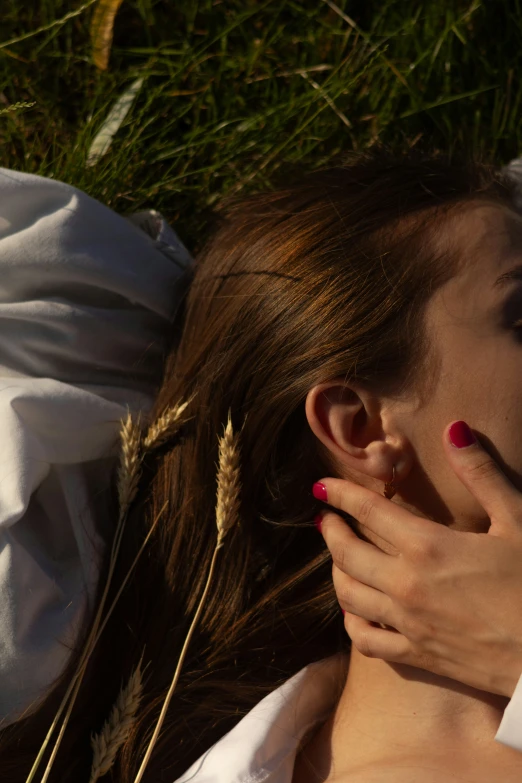 a woman's head lies in the grass with her hands on her face