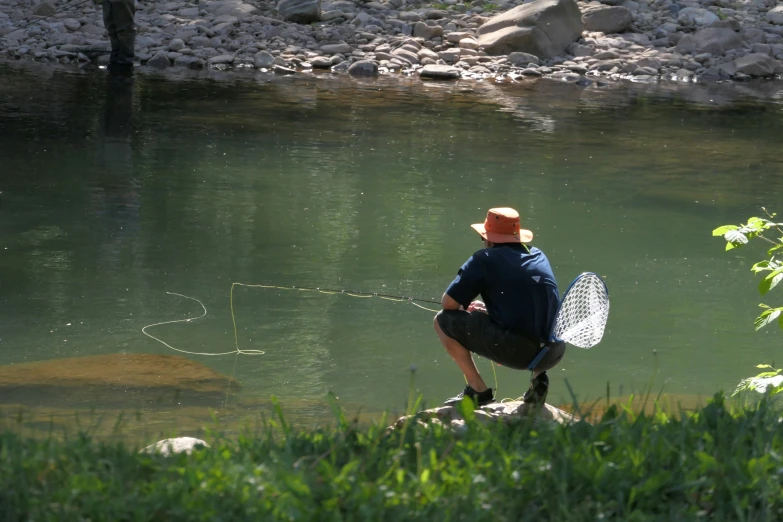 a man with a fishing net crouching next to a body of water