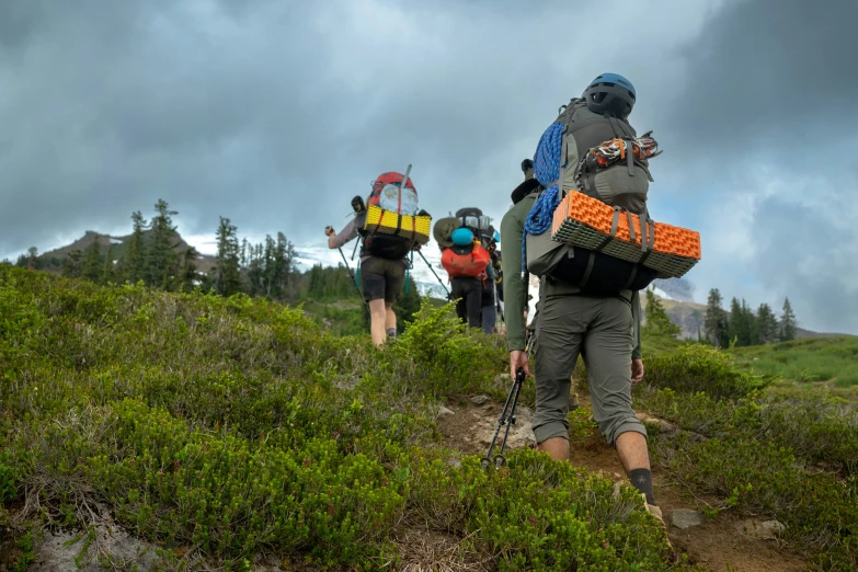 three hikers with their packs trekking up a hill