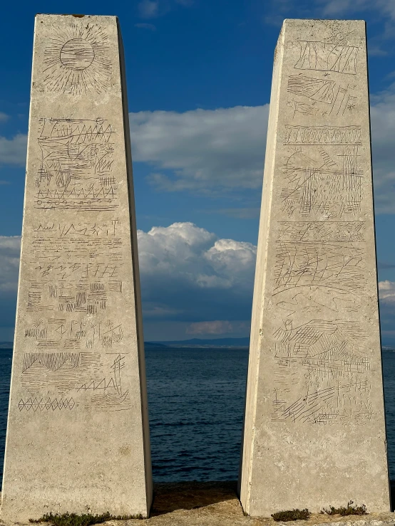 two stone statues with writing on them in front of the water